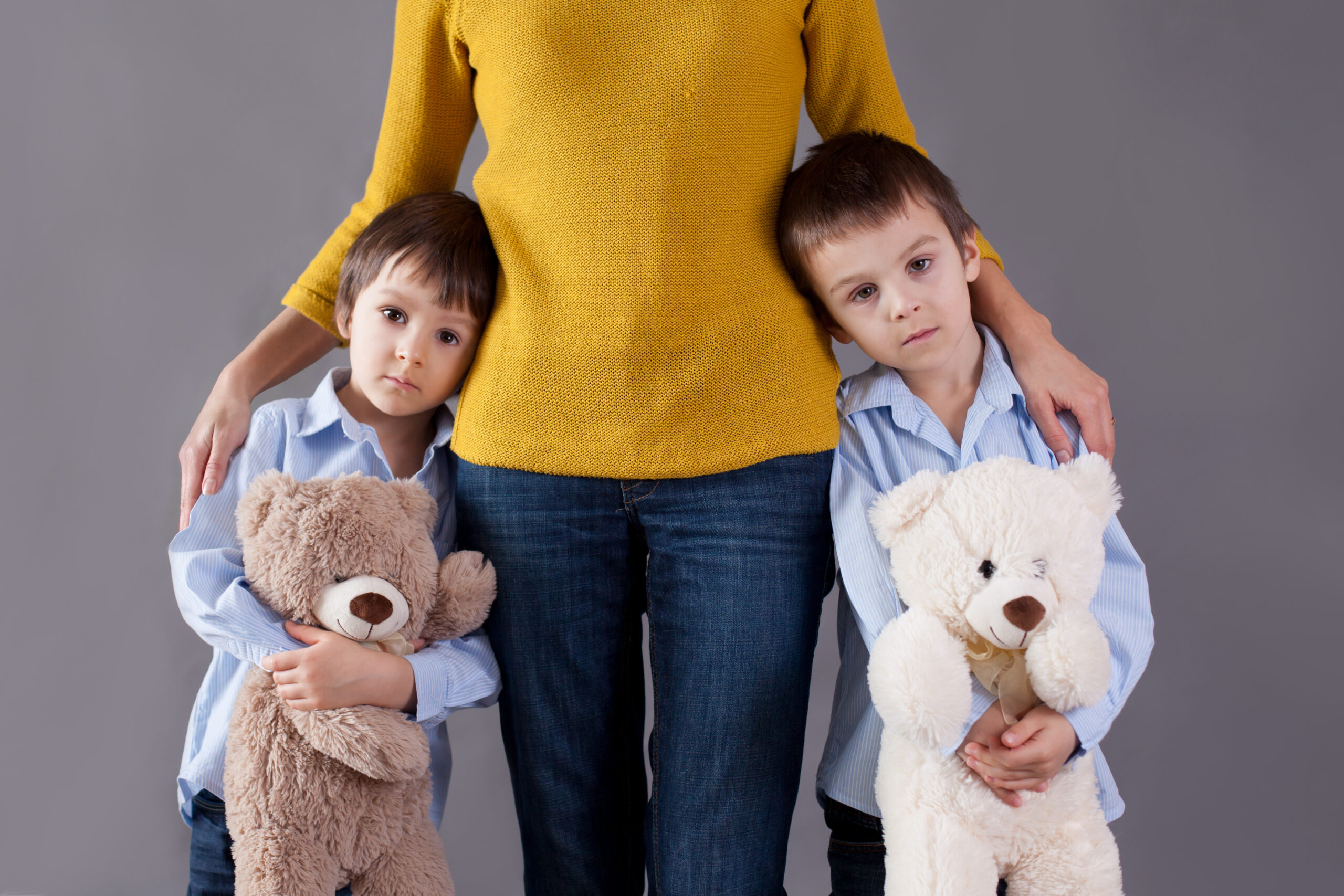 Two small children with teddy bears leaning on a woman, who can be their mother or legal guardian. 